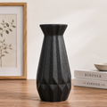 Black modern ceramic decorative vase with a geometric textured finish displayed on a wooden table in a minimalist Scandinavian-style home interior.