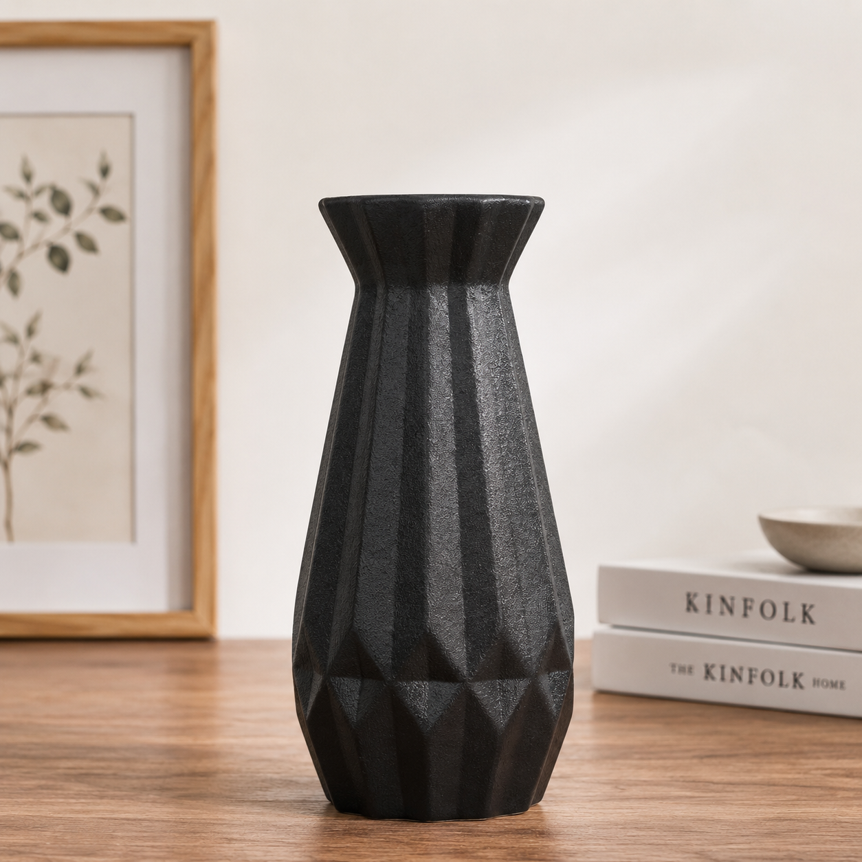 Black modern ceramic decorative vase with a geometric textured finish displayed on a wooden table in a minimalist Scandinavian-style home interior.