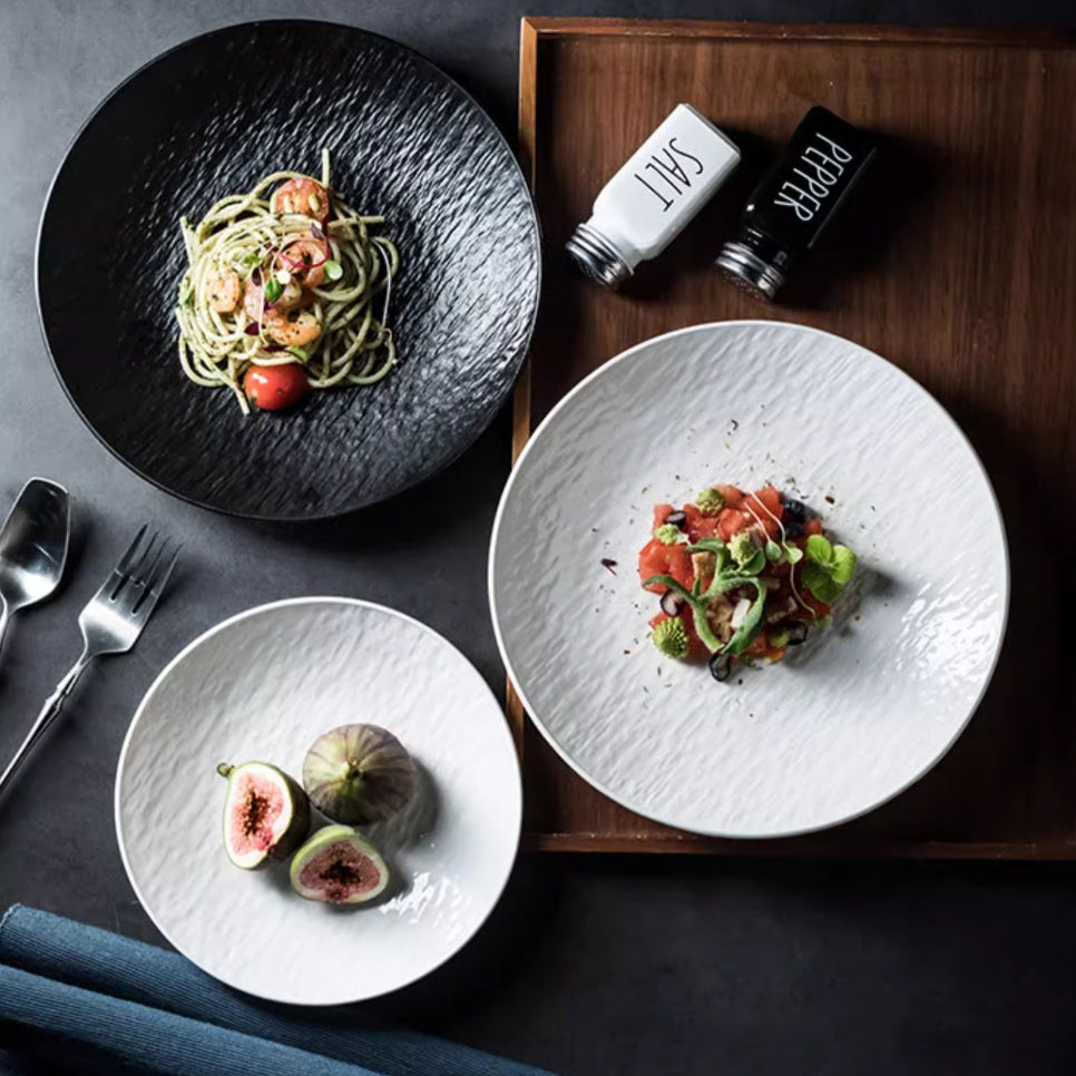 Black and white textured ceramic dinner plates styled with gourmet food on a modern dining table